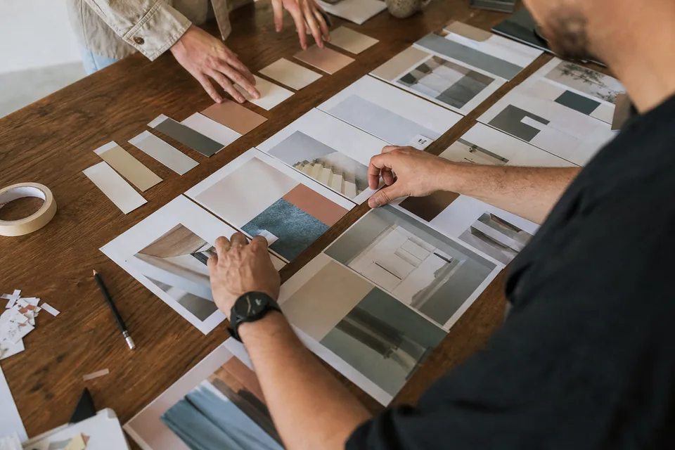 Hands arranging printed web layouts and color swatch cards into rows on a studio table
