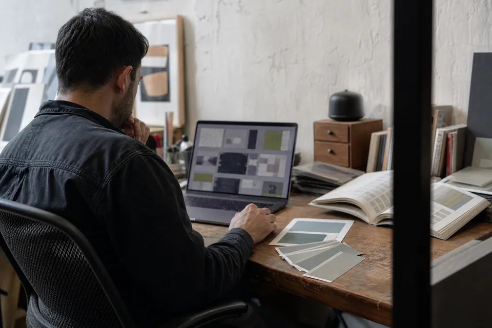 Brand designer reviewing a grid of website screenshots next to color swatches and a type specimen book